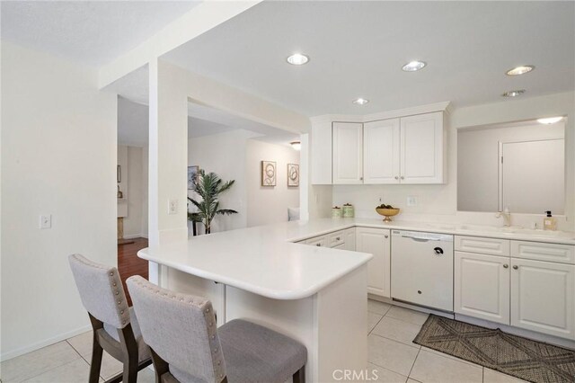 kitchen with a peninsula, a kitchen bar, light tile patterned floors, and dishwasher