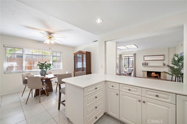 kitchen featuring white cabinets, a warm lit fireplace, light countertops, baseboards, and light tile patterned floors