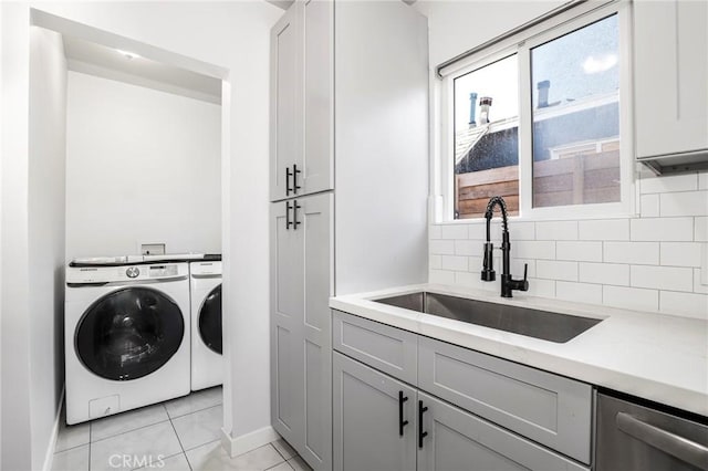 laundry area featuring light tile patterned floors, washer and clothes dryer, baseboards, and a sink
