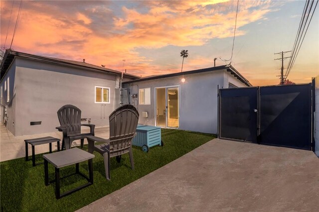 rear view of property with a yard, stucco siding, a gate, and a patio area