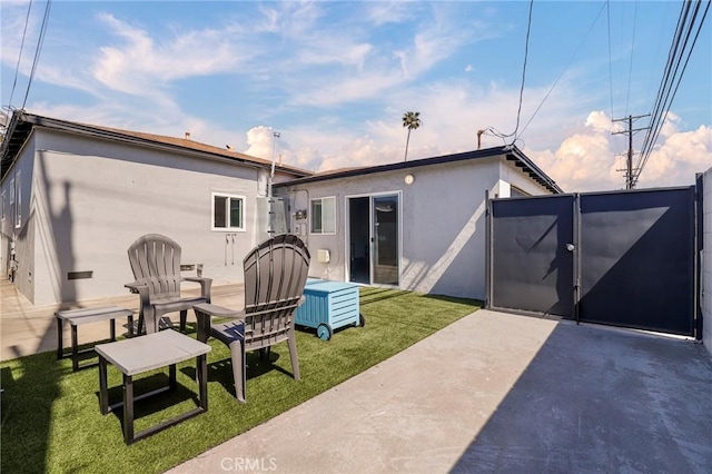 back of property featuring stucco siding, a gate, a patio area, and a lawn