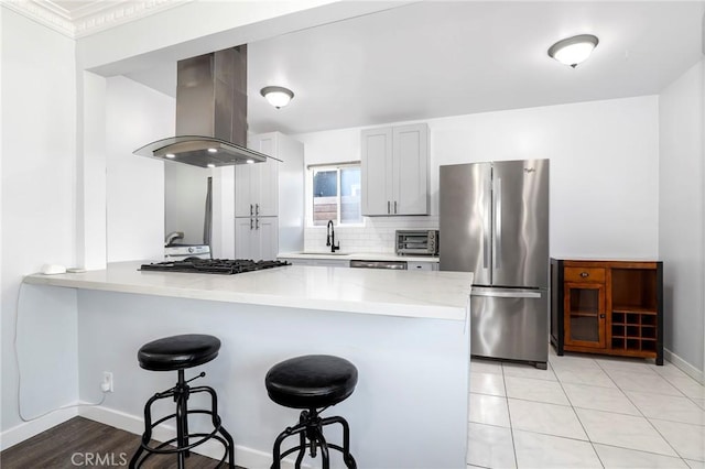 kitchen with a sink, island exhaust hood, a kitchen breakfast bar, a peninsula, and freestanding refrigerator