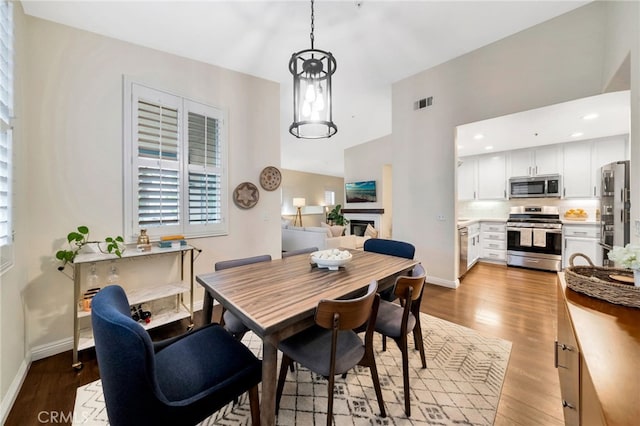 dining area featuring baseboards, a fireplace, wood finished floors, and visible vents