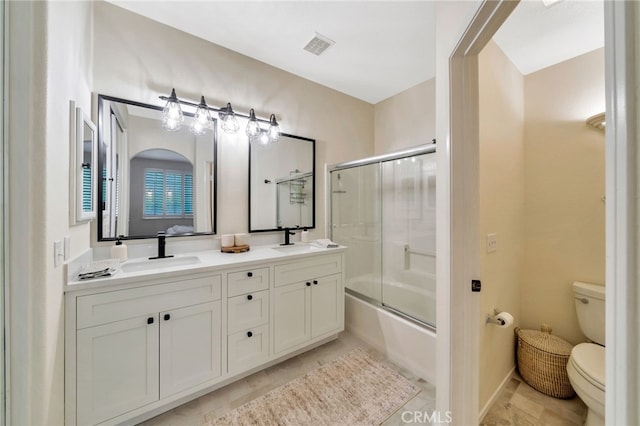 full bath featuring a sink, bath / shower combo with glass door, toilet, and double vanity