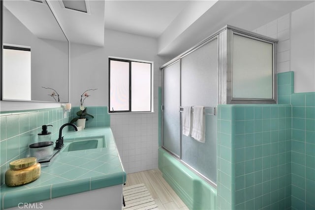 bathroom with wainscoting, vanity, shower / bath combination with glass door, and tile walls