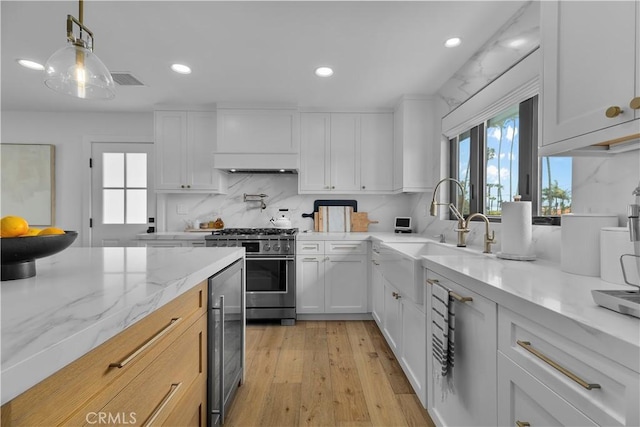 kitchen with high end stainless steel range oven, white cabinetry, a sink, light wood finished floors, and wine cooler