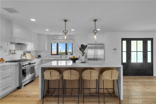 kitchen with high end appliances, a center island, visible vents, premium range hood, and white cabinets