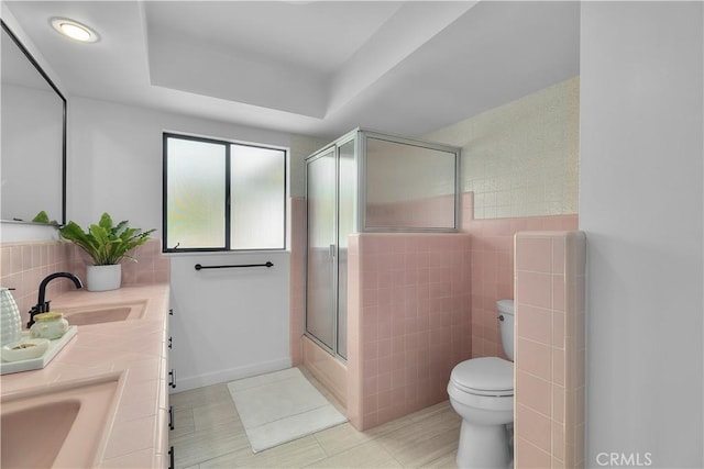 bathroom with shower / bath combination with glass door, tile walls, a sink, toilet, and tile patterned flooring