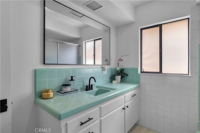 full bathroom featuring a shower with door, tile walls, vanity, and plenty of natural light