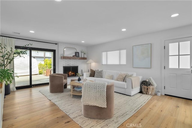 living room featuring a healthy amount of sunlight, light wood-type flooring, and a brick fireplace
