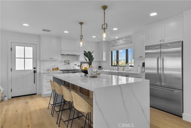 kitchen featuring a sink, tasteful backsplash, stainless steel built in fridge, light stone counters, and white cabinetry