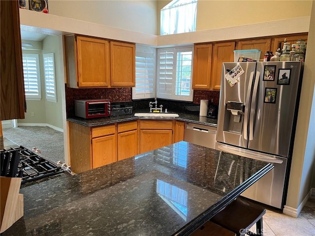 kitchen with decorative backsplash, a toaster, dark stone counters, a sink, and appliances with stainless steel finishes