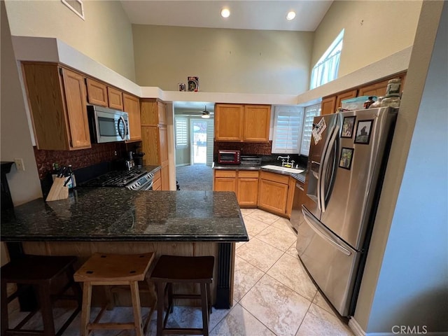 kitchen with a peninsula, a high ceiling, light tile patterned floors, appliances with stainless steel finishes, and backsplash