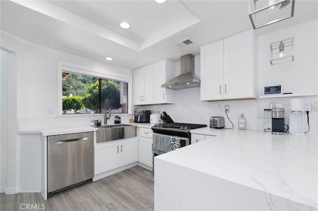 kitchen featuring a sink, appliances with stainless steel finishes, white cabinets, and wall chimney range hood