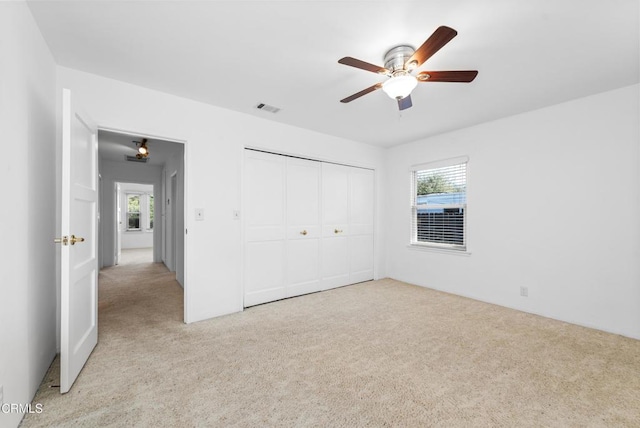 unfurnished bedroom featuring visible vents, light carpet, ceiling fan, and a closet