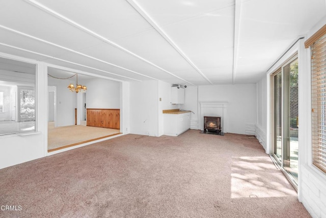 unfurnished living room featuring an inviting chandelier, wooden walls, a wainscoted wall, and carpet floors