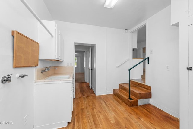 kitchen with white cabinets, light wood-type flooring, light countertops, and a sink