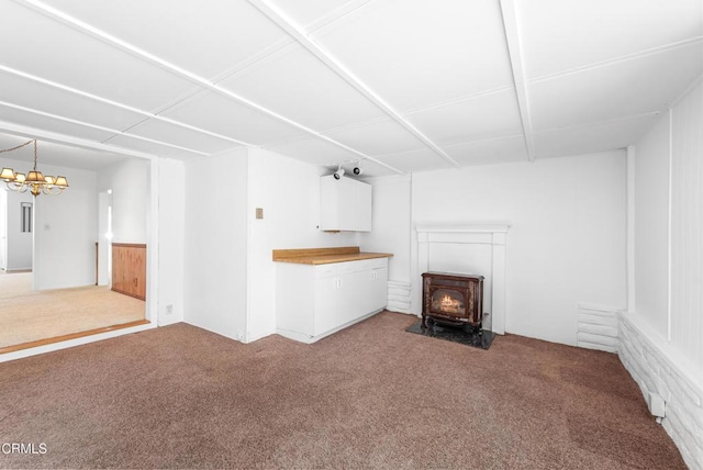 unfurnished living room featuring a wood stove, a chandelier, and carpet