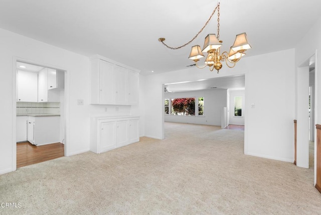 unfurnished living room featuring baseboards, light carpet, and an inviting chandelier