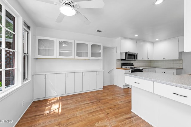 kitchen with stainless steel microwave, decorative backsplash, white cabinets, glass insert cabinets, and gas range gas stove