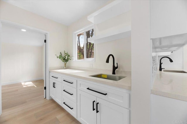 kitchen with open shelves, a sink, light wood finished floors, white cabinetry, and baseboards