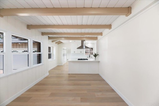 hallway with light wood-style floors, baseboards, and beam ceiling
