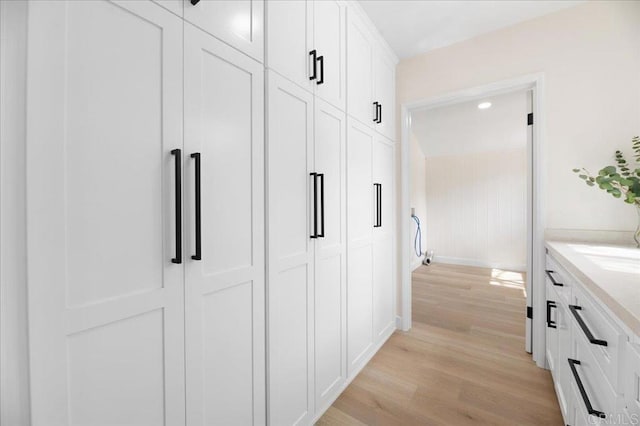 hall featuring light wood finished floors, baseboards, and a sink
