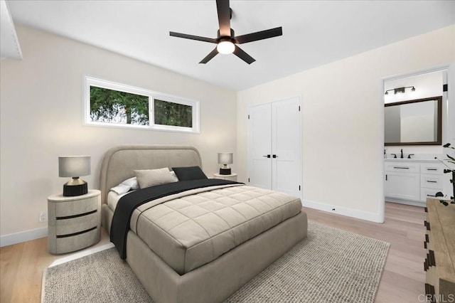bedroom featuring light wood finished floors, baseboards, a closet, and ensuite bath