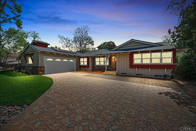 view of front of home with board and batten siding, decorative driveway, a garage, a chimney, and a lawn