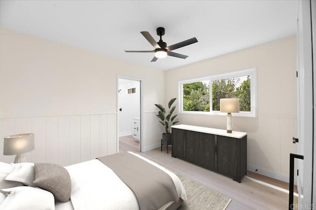 bedroom featuring light wood-style flooring, a wainscoted wall, and ceiling fan