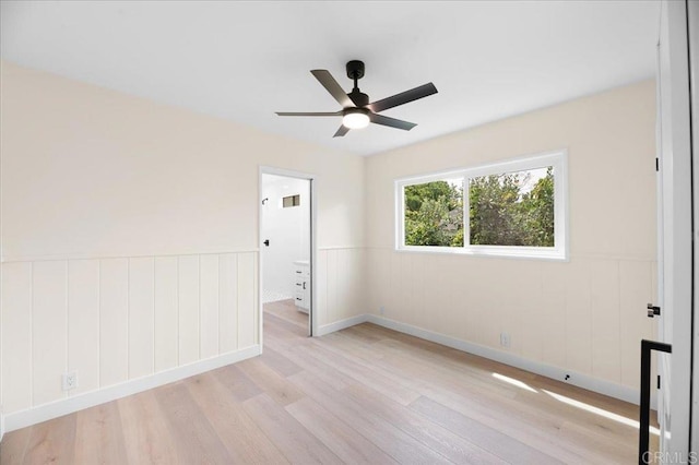 spare room featuring light wood-style floors, a ceiling fan, and wainscoting