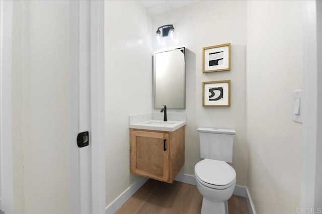 half bath with vanity, wood finished floors, toilet, and baseboards
