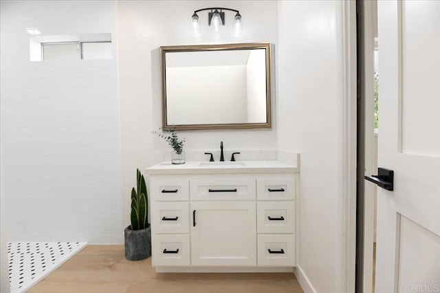 full bath featuring vanity, wood finished floors, a tile shower, and baseboards