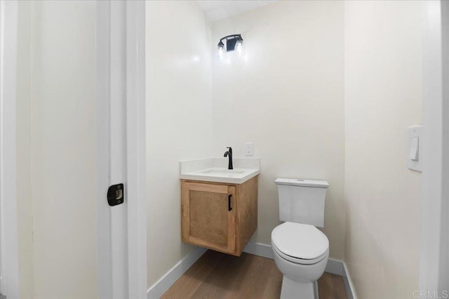 bathroom with toilet, wood finished floors, vanity, and baseboards