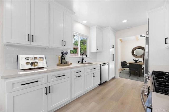 kitchen with stainless steel appliances, a sink, white cabinets, light countertops, and backsplash