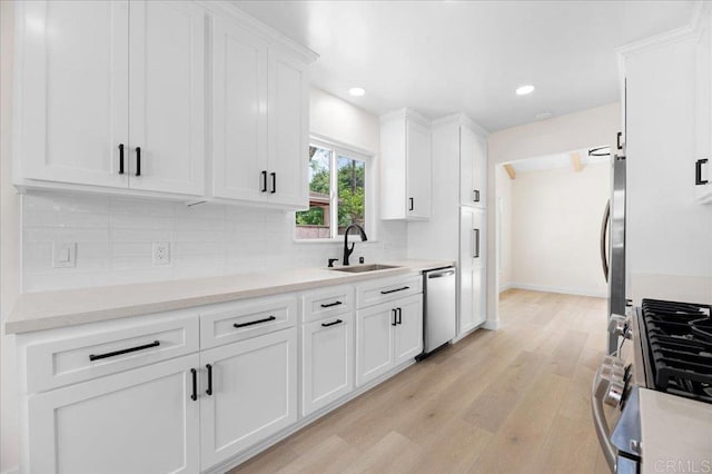 kitchen with appliances with stainless steel finishes, a sink, white cabinets, light wood finished floors, and decorative backsplash