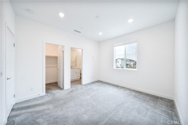 unfurnished bedroom featuring visible vents, baseboards, carpet flooring, and a walk in closet