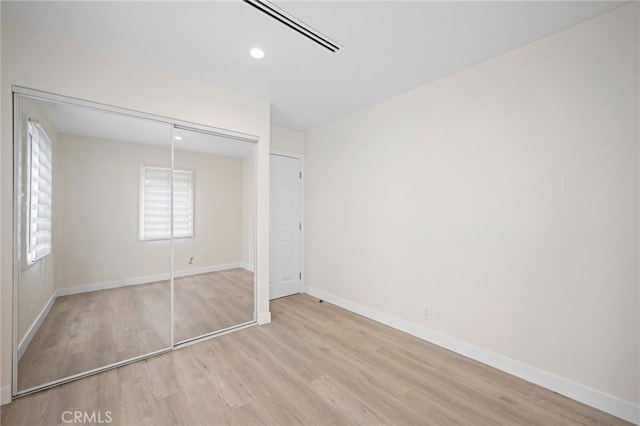 unfurnished bedroom featuring baseboards, recessed lighting, wood finished floors, and a closet