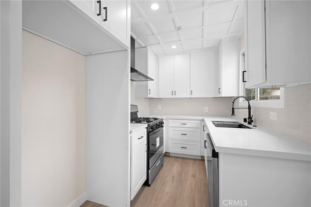 kitchen with a sink, light wood-type flooring, wall chimney exhaust hood, light countertops, and gas range