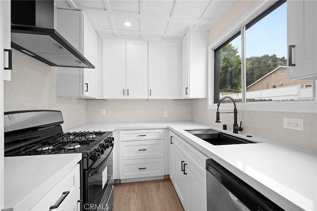 kitchen with stainless steel dishwasher, white cabinets, a sink, black gas range, and wall chimney exhaust hood