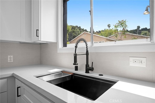 room details featuring light countertops, a sink, white cabinetry, and tasteful backsplash