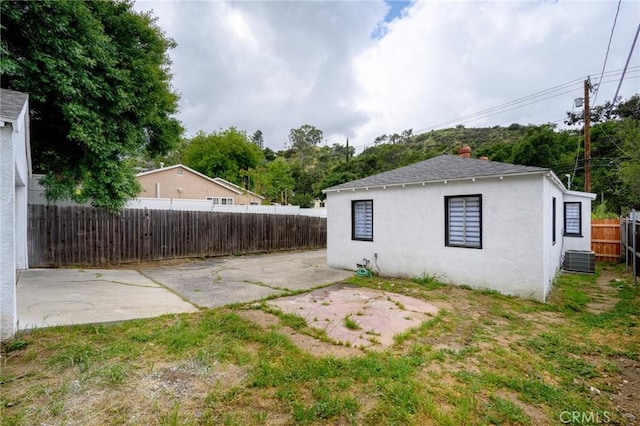 view of side of home featuring stucco siding, central AC unit, a patio, and a fenced backyard