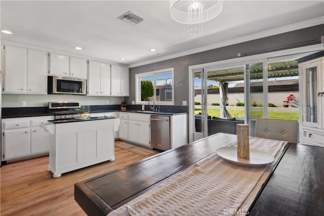 kitchen with crown molding, white cabinets, a sink, stainless steel appliances, and visible vents