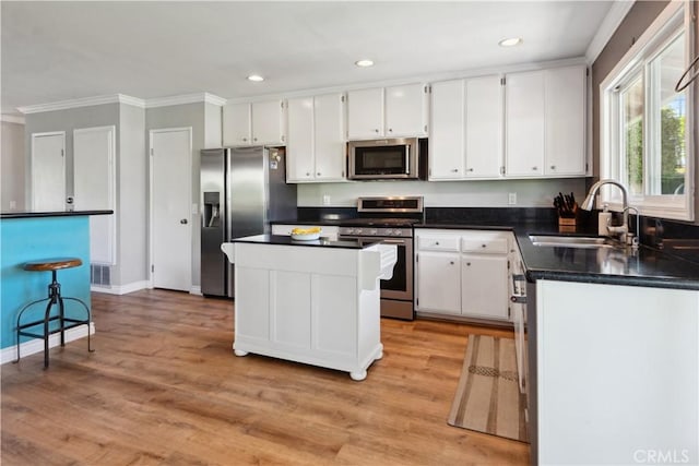 kitchen with white cabinets, dark countertops, a sink, stainless steel appliances, and ornamental molding