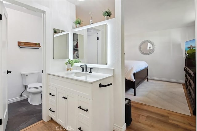 bathroom featuring wood finished floors, vanity, baseboards, toilet, and connected bathroom