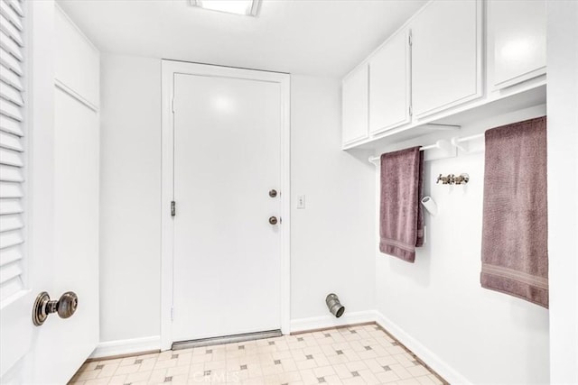 clothes washing area with baseboards, light floors, and cabinet space