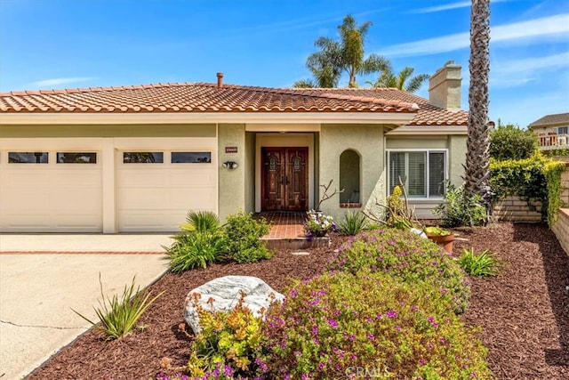 mediterranean / spanish home with a garage, stucco siding, a chimney, a tiled roof, and driveway