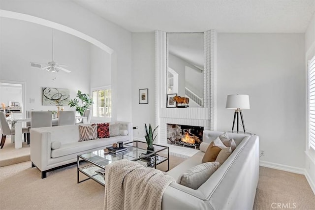 living area featuring visible vents, a brick fireplace, light carpet, baseboards, and a ceiling fan