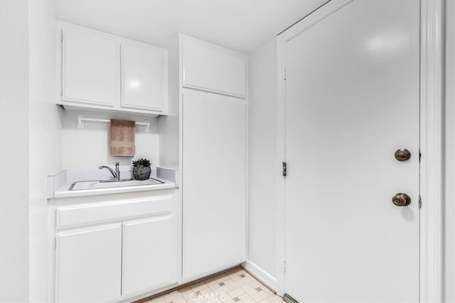 kitchen featuring light floors, light countertops, a sink, and white cabinets