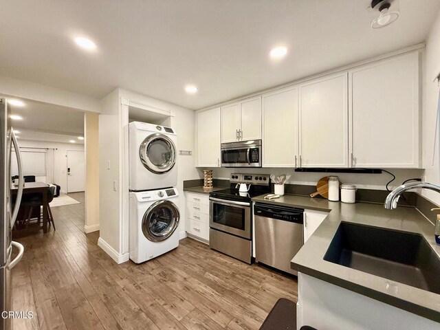 kitchen featuring stacked washer and dryer, white cabinetry, a sink, light wood-style flooring, and stainless steel appliances